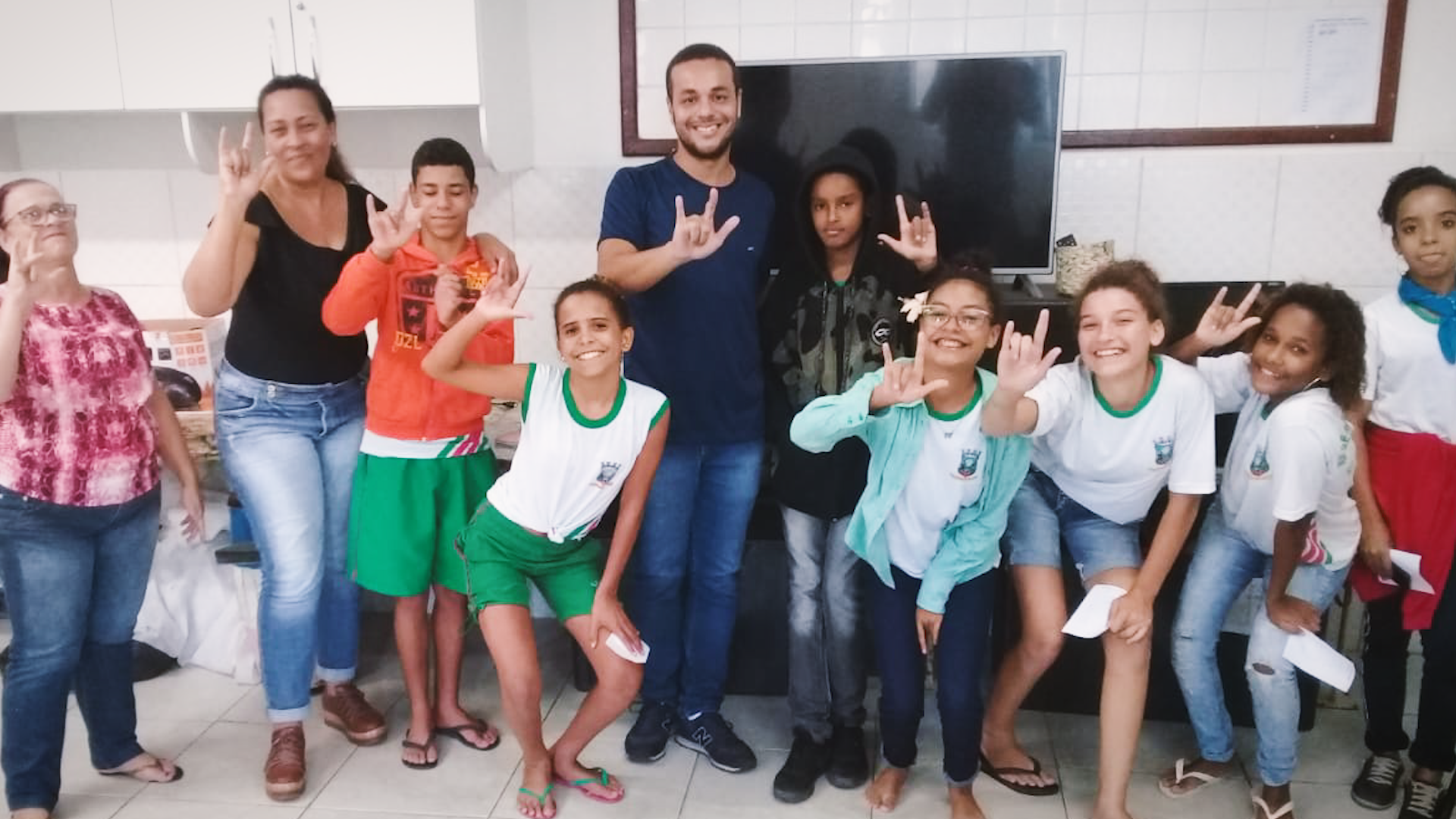 Preview image for the video "Ensina Brasil alumnus André Liboreiro is using research to dismantle structural racism in education" - A young male teacher and a group of young teenagers smile and show peace signs.