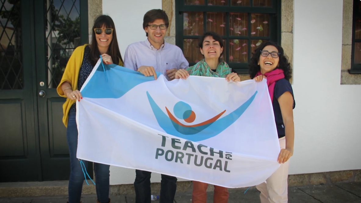Preview image for the video "Early stage support video" - A man and three women, all white with brown hair, smile while holding a flag that says Teach For Portugal.