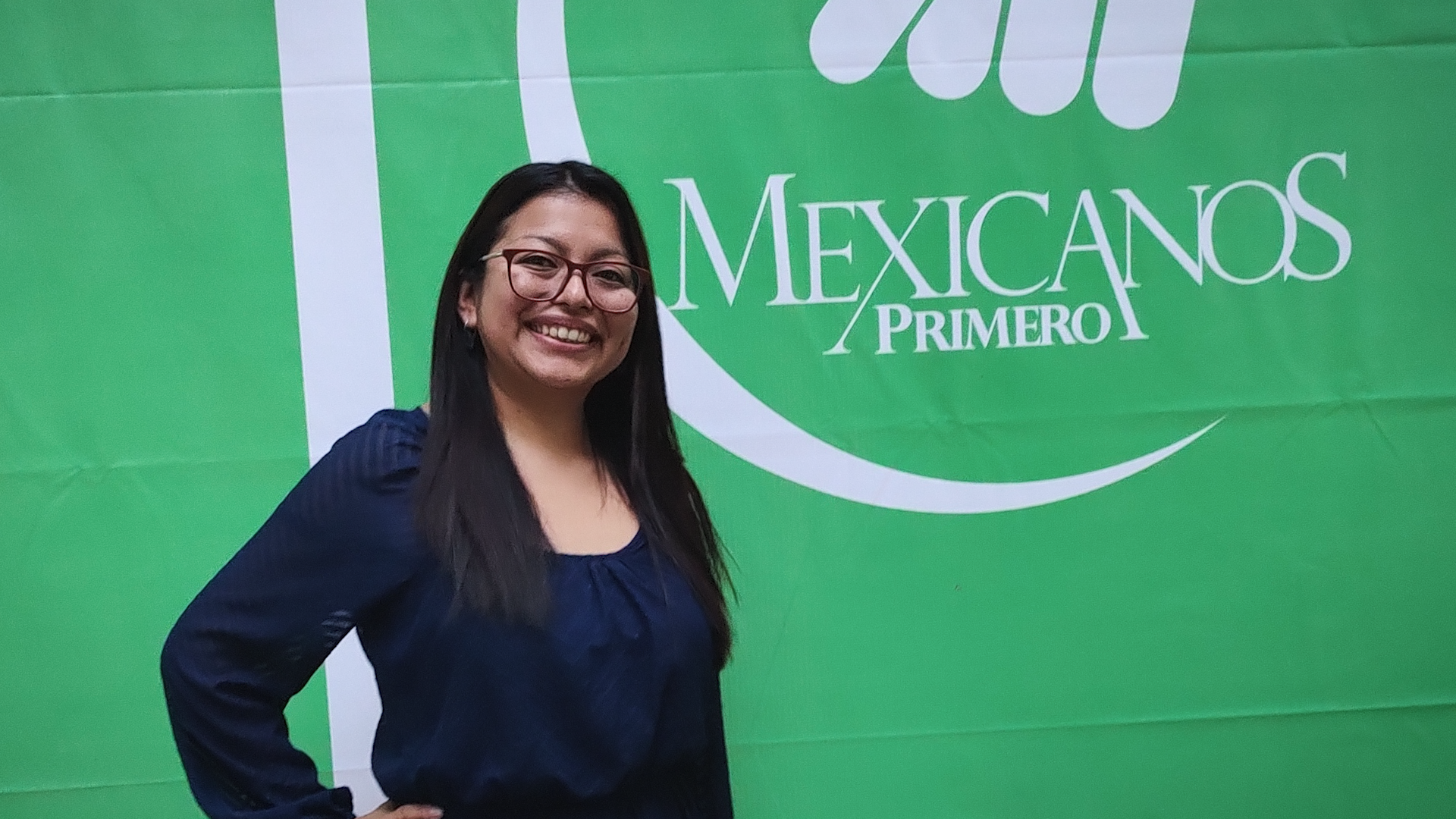 Preview image for the video "Enseña por México alumna Angélica Montes believes deeply in the transformational power of education" - A young woman with long brown hair and glasses stands in front of a green sign that says Mexicanos Primero.