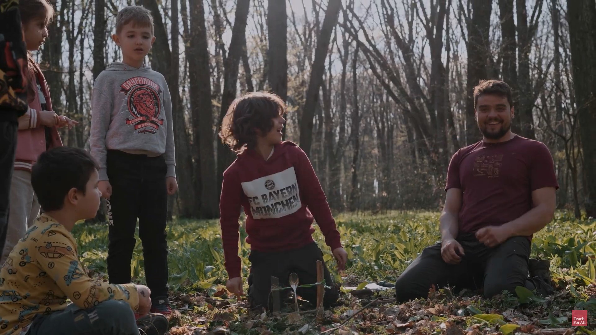 Preview image for the video "In Romania, Andrei Barbos Niculescu is helping his students see that nature is the greatest teacher" - Three children and a young man with a beard are out in the woods smiling.