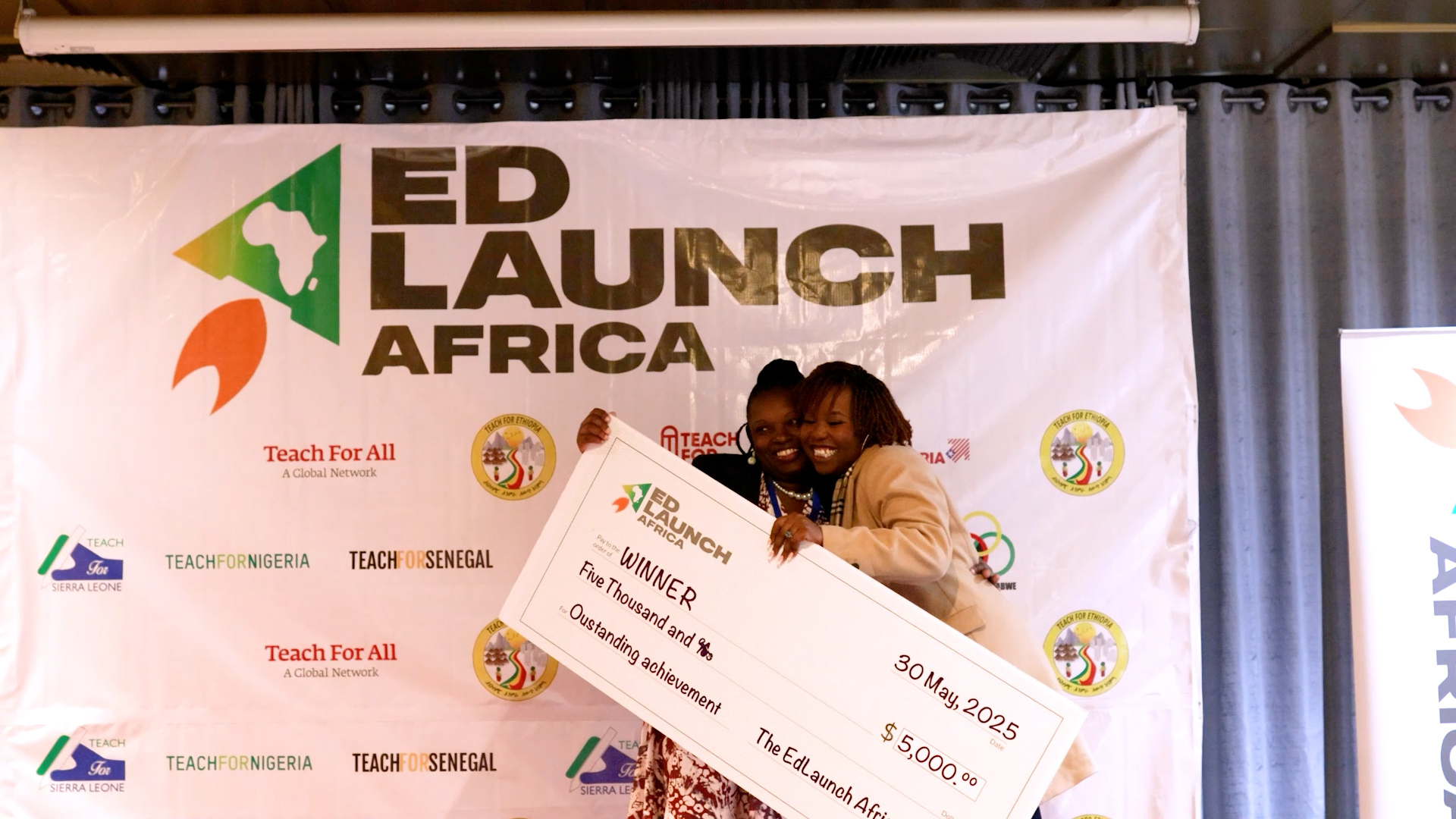 Preview image for the video "EdLaunch Africa 2025" - Two Black women hug while holding a giant check in front of a backdrop that says EdLaunch Africa.
