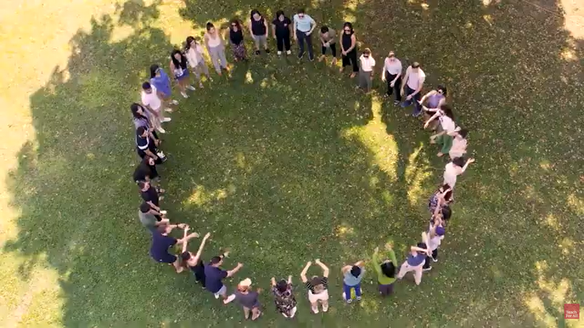 Preview image for the video "Cumbre de Acción Sobre Educación Climática 2025" - Overhead shot of a group of people standing in a circle on a green lawn with their arms raised.
