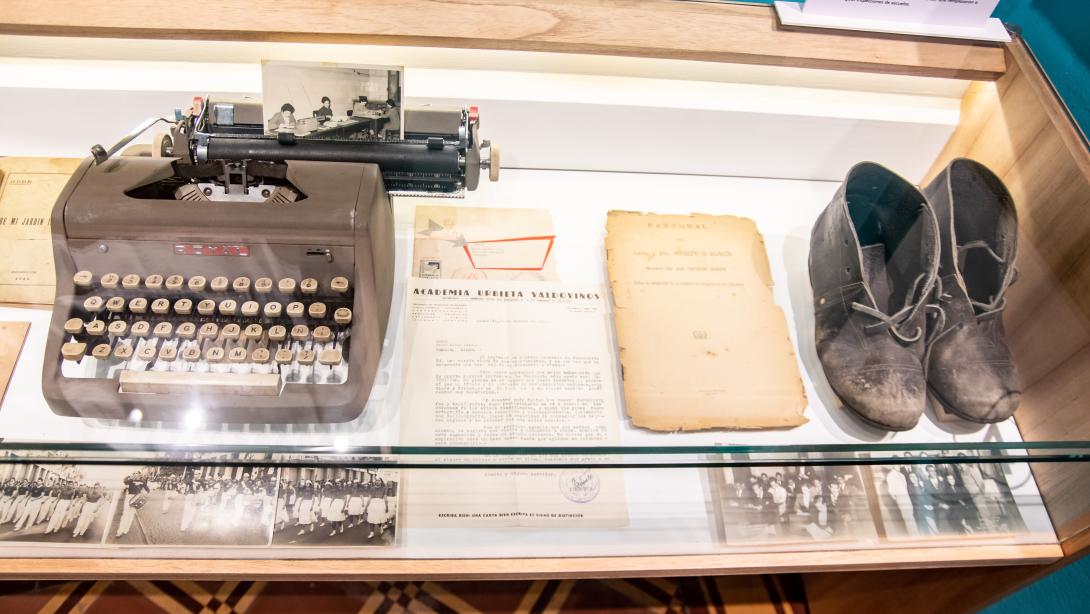Museum display case with a typwriter, document and shoes inside
