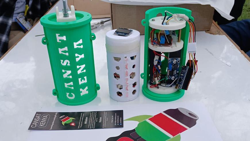 Three 3D-printed CanSat satellite components, labeled "CANSAT KENYA," showing the green outer casing, white inner payload, and internal electronic circuitry.