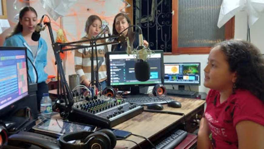 Three young girls and their teacher gather around recording equipment in a radio studio